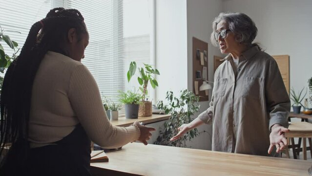 Coffee shop worker listening to one of angry customers complaining about her drink and leaving it on table