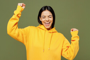 Young overjoyed excited happy fun Latin woman wearing yellow hoody casual clothes doing winner gesture clench fist say yes isolated on plain pastel green background studio portrait. Lifestyle concept.
