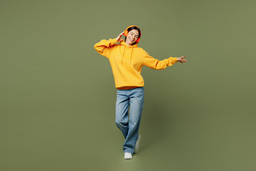Full body young fun Latin woman she wears yellow hoody casual clothes listen to music in headphones raise up hands dance isolated on plain pastel green background studio portrait. Lifestyle concept.