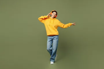 Gardinen Full body young fun Latin woman she wears yellow hoody casual clothes listen to music in headphones raise up hands dance isolated on plain pastel green background studio portrait. Lifestyle concept. © ViDi Studio