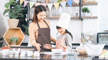 Happy asian family mother and daughter cooking in kitchen bake cake at home