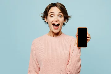Deurstickers Young surprised woman wear beige knitted sweater casual clothes hold in hand use blank screen mobile cell phone chatting online isolated on plain pastel light blue cyan background. Lifestyle concept. © ViDi Studio