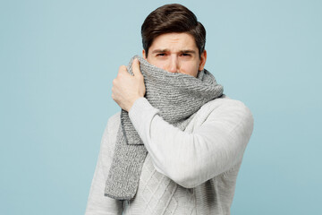 Young sad tired exhausted ill sick man in gray sweater cover mouth with scarf isolated on plain blue background studio portrait. Healthy lifestyle disease virus treatment cold season recovery concept. - obrazy, fototapety, plakaty