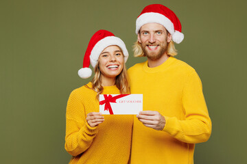 Merry young couple two friends man woman wear sweater Santa hat posing hold gift certificate coupon...