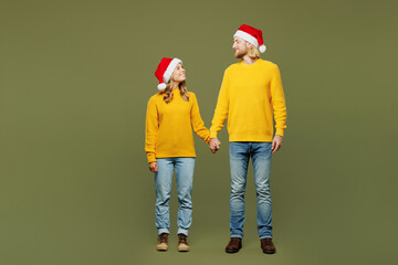Full body fun merry young couple two friends man woman wear sweater Santa hat posing hold hands...