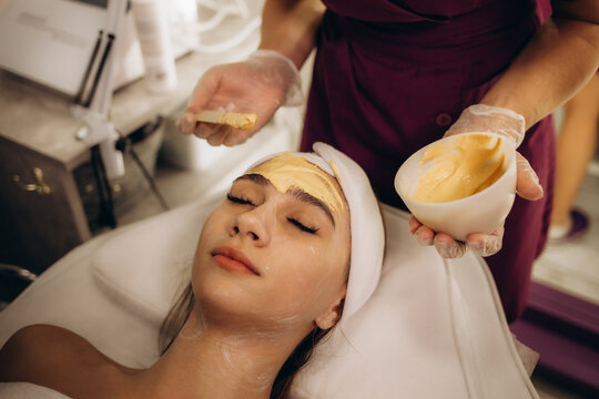 a beautician applies a yellow alginate mask to a woman
