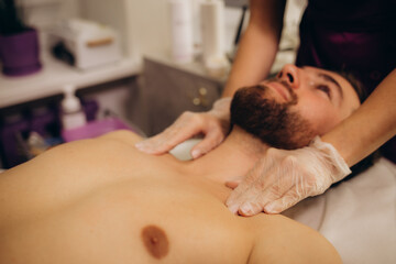 Fototapeta na wymiar Masseur giving neck massage to young wealthy caucasian athlete in dark room of spa salon