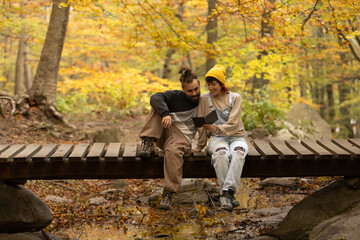 male and female couple reading an ebook in the forest with sitting on a bridge