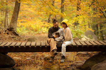 Fototapeta premium male and female couple reading an ebook in the forest with sitting on a bridge