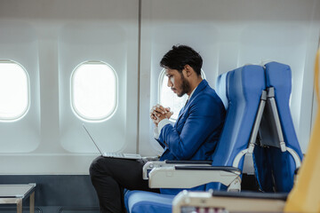 Young businessman sitting in airplane using laptop and smart phone