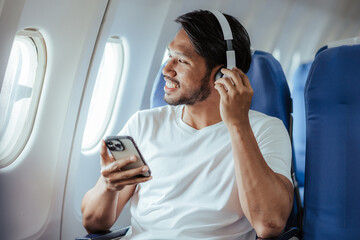 Male tourist using a mobile phone while on the plane - obrazy, fototapety, plakaty