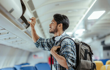 Male tourist traveling by plane Passengers place their carry-on luggage in lockers above their...