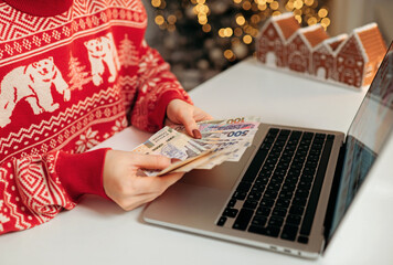 Woman counting ukrainian hryvnia bills, using laptop. Woman estimating money balance for shopping...