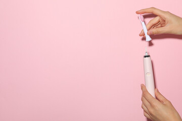 Electric toothbrush in female hands on pink background, space for text