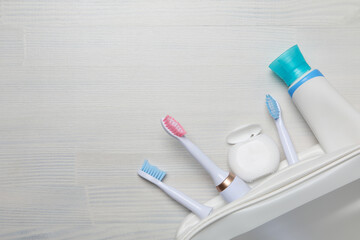 Electric toothbrushes, dental floss, tube in cosmetic bag on white wooden background, space for text