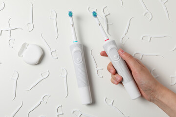 Electric toothbrushes in hand and dental floss on white background, top view