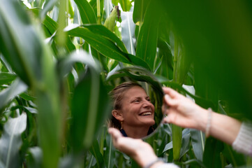 Young woman looks and smiles in a round mirror against the background of a green corn field