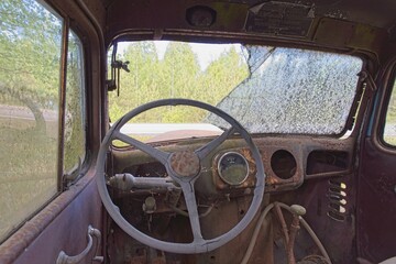 Closeup of an steering wheel with front window broken on an abandoned car.