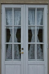 Closeup of glass windows with curtains on a white wood door on a building.