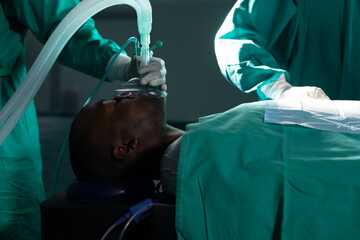 Diverse surgeons wearing surgical gowns using anaesthetic mask in operating theatre at hospital