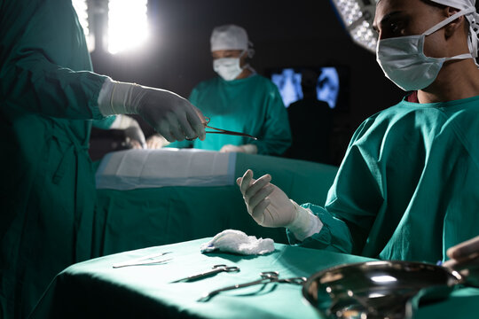 Diverse surgeons wearing surgical gowns using surgical instruments in operating theatre at hospital
