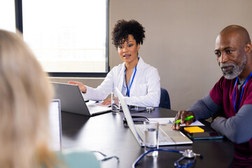Happy diverse male and female medical staff with laptops talking at office meeting