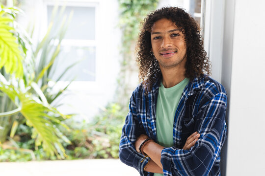Happy biracial man with long dark curly hair smiling in sunny living room at home