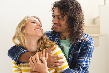 Happy diverse couple embracing and smiling in sunny living room at home, copy space