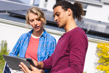 Happy diverse couple installing solar panels and using tablet in sunny garden, copy space