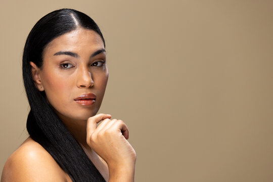 Portrait of biracial woman with dark hair and natural make up on brown background, copy space