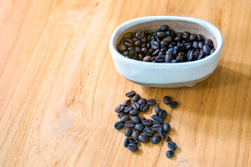 Coffee beans roasted in a ceramic bowl and spread on wooden table background. suitable for both hot and cold coffee. Soft and selective focus.  