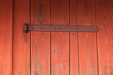 Closeup of a old rusty metal door hinge on a red wood building.
