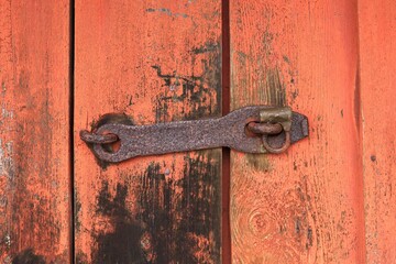 Closeup of a old rusty metal latch with padlock on a red wood building.
