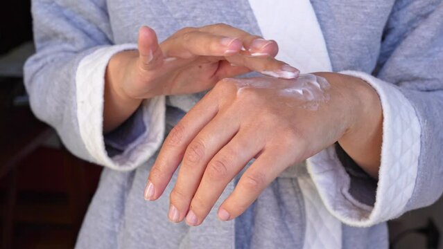 A woman applies hand moisturizer to the skin of her hands