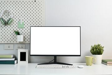 Blank computer monitor, coffee cup, houseplant and stationery on white table with peg board on wall