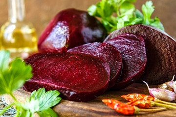Sliced boiled beets on a dark wooden background. Slices of boiled red beetroot, garlic, red hot pepper and parsley lie on a wooden table.