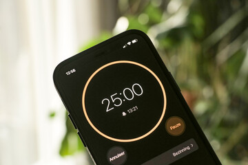 A phone with a black and orange 25-minute timer to study with the pomodoro method on a blurry background