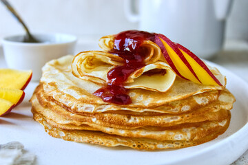 A stack of pancakes with jam on a white ceramic plate. Pancakes with jam and nectarines on a light background. Pancakes on a white plate, selective focus. Russian traditions. Russian holiday. Maslenit