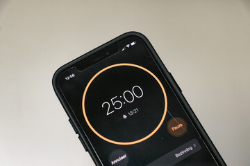 A phone with a black and orange 25-minute timer to study with the pomodoro method on a white blurry...