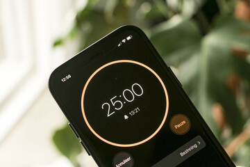 A phone with a black and orange 25-minute timer to study with the pomodoro method on a blurry background