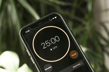 A phone with a black and orange 25-minute timer to study with the pomodoro method on a blurry background