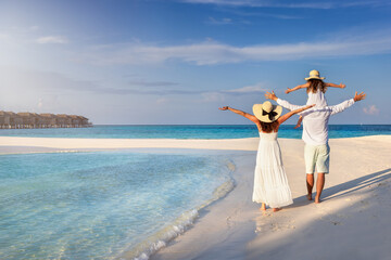A happy family walks down a tropical beach as a concept for a beach holiday - obrazy, fototapety, plakaty
