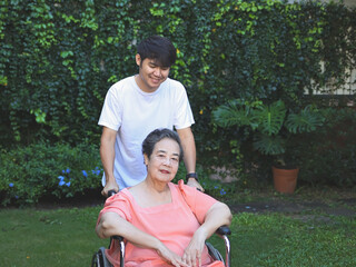 Obraz premium Asian senior woman sitting on wheelchair with her son in the garden.