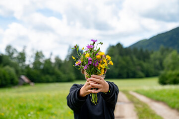 Teenaged boy holding beautiful colorful bouquet of hand picked meadow flowers directly towards the...