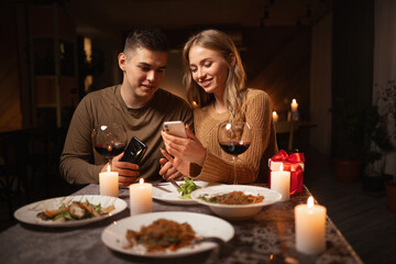 Happy young couple in love looking photos on smartphone during romantic dating or celebrating valentine's day at home
