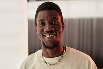 Front view portrait of young Black man looking at camera and smiling with tooth gap against minimal background, copy space