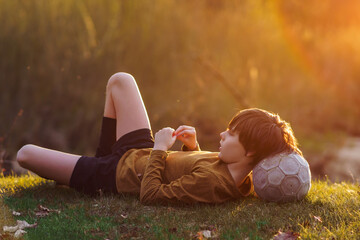 Waiting for workout in summer morning at sports camp. Teenager lies on mown grass , resting his head on soccer ball.