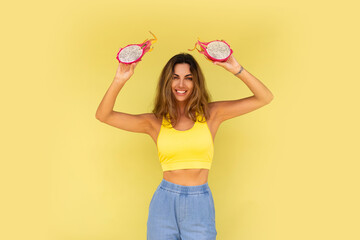 Pretty brunette woman posing with tropical fruits over yellow background. Summer vibes.