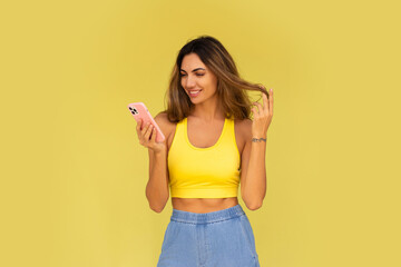Pretty brunette woman posing with mobyle phone  over yellow background. Casual stylish outfit.
