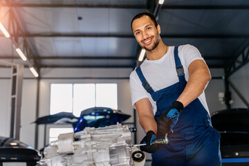 Portrait of smiling handsome male mechanic repairs motor of electric car automobile in workshop. Automobile service, repair, maintenance and people concept.